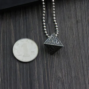 Dark oxidized sterling silver pyramid pendant with bead chain on wooden surface with coin size reference, overhead view