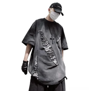 Oversized distressed gothic ripped T-shirt in charcoal gray with diagonal frayed patches, front three-quarter view on male model