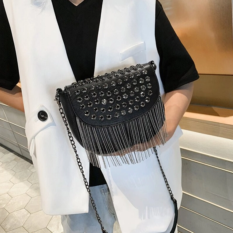 Woman styling black gothic studded shoulder bag with chain strap, three-quarter front view in modern retail space
