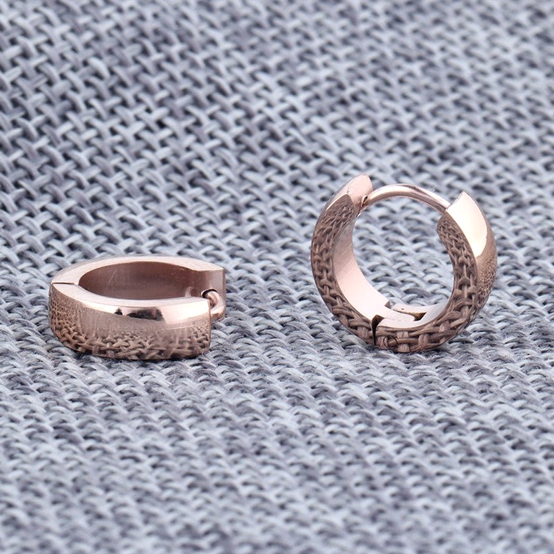 Rose gold textured huggie hoop earrings with embossed grid pattern and hinged snap closure on fabric background