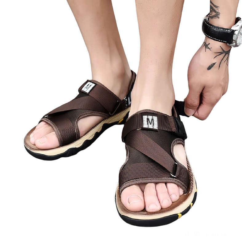 Male model wearing dark brown gothic buckle sandals with wrist tattoo, studio front view