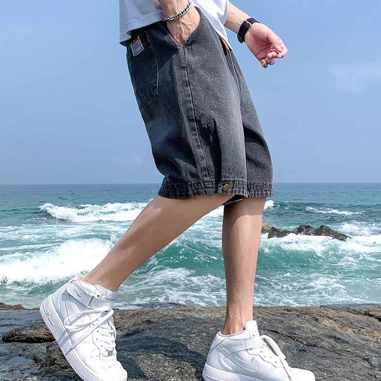 Side profile of male model in dark grey gothic denim shorts with white casual sneakers at rocky beach