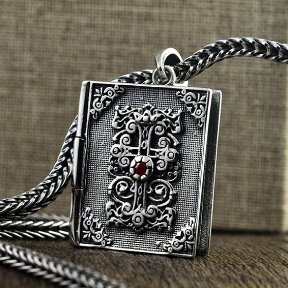 Sterling silver bible locket pendant on twisted silver chain necklace with red gemstone cross accent, worn display on wooden backdrop