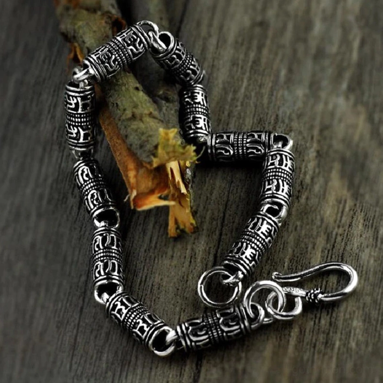 Sterling silver engraved cylindrical bracelet chain detail, low angle close-up on wooden surface highlighting aged tube beads and hook clasp