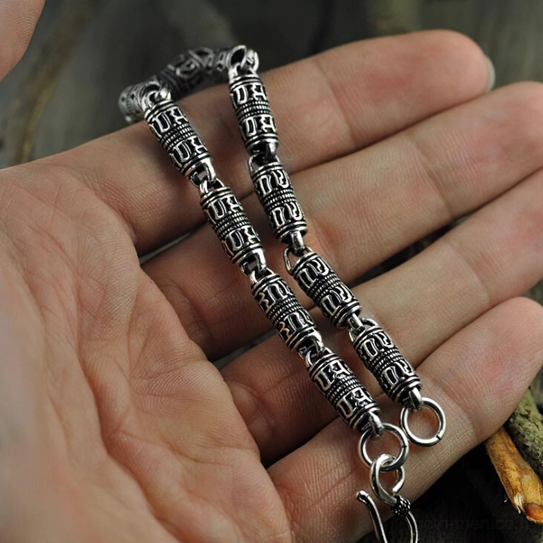 Silver engraved cylindrical bracelet in hand, eye-level close-up view showcasing intricate carved patterns and hook closures with natural lighting