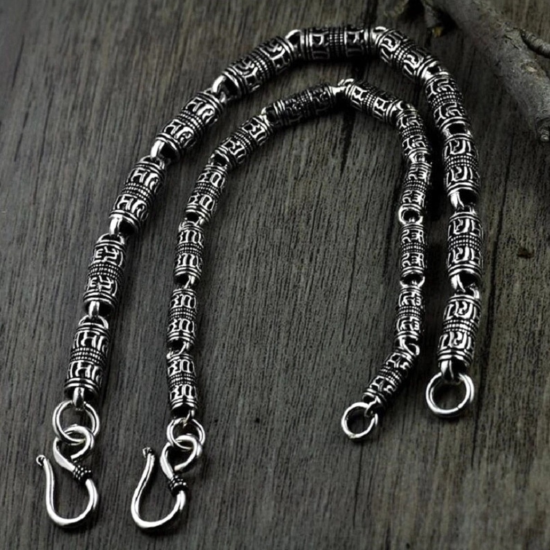 Matching pair of gothic silver engraved cylindrical bracelets with carved beads, overhead view on dark wooden background with vintage aesthetic