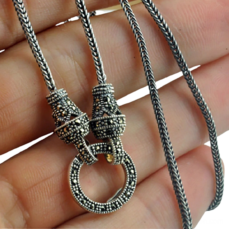Antique silver pendant necklace with marcasite inlaid clasp held in hand, close-up detail view showing oxidized finish and engraved connector
