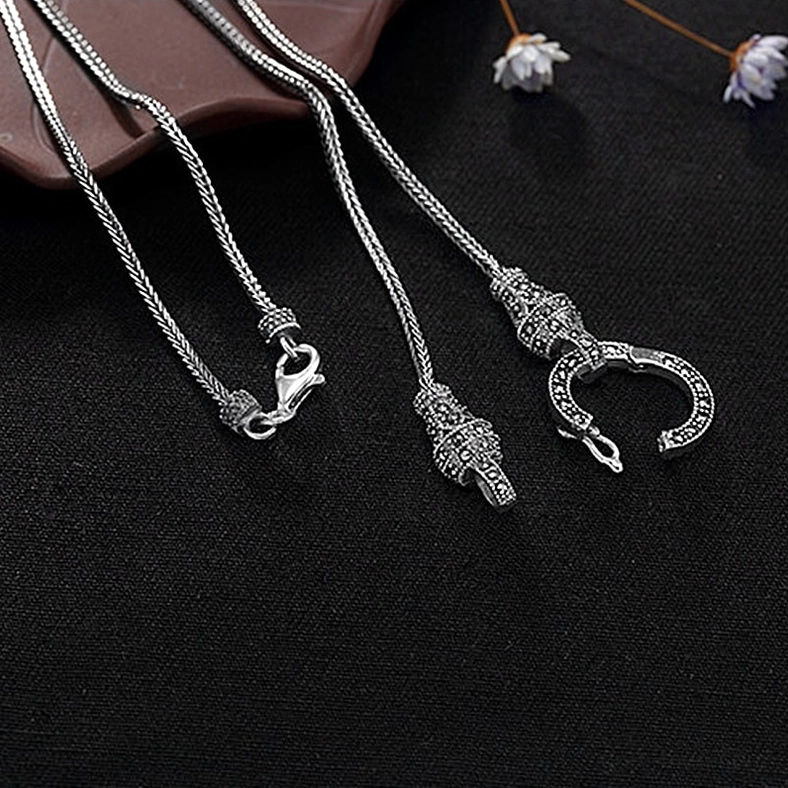 Two antique gothic silver chain necklaces overhead flat lay on black background with decorative flower props, showing braided chain and vintage clasp styles