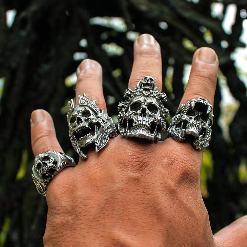 Multiple stainless steel gothic skull biker rings worn on hand, aged dark metal finish, outdoor setting