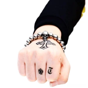 Skull beaded bracelet worn on tattooed male hand black sleeve dark backdrop gothic fashion styling