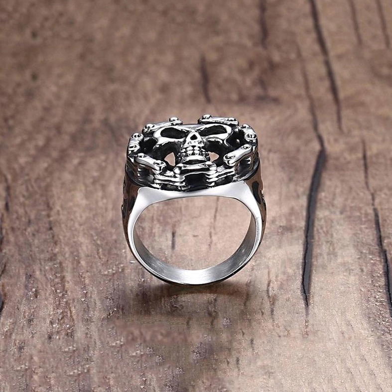 Stainless steel gothic skull ring side profile on wooden surface, cross cutout and detailed skull relief visible