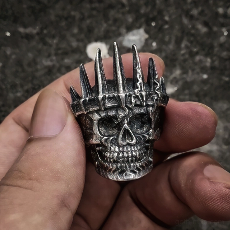 Skull crown gothic ring top front view between fingers dark stone background showing intricate carved skull and spiked crown details