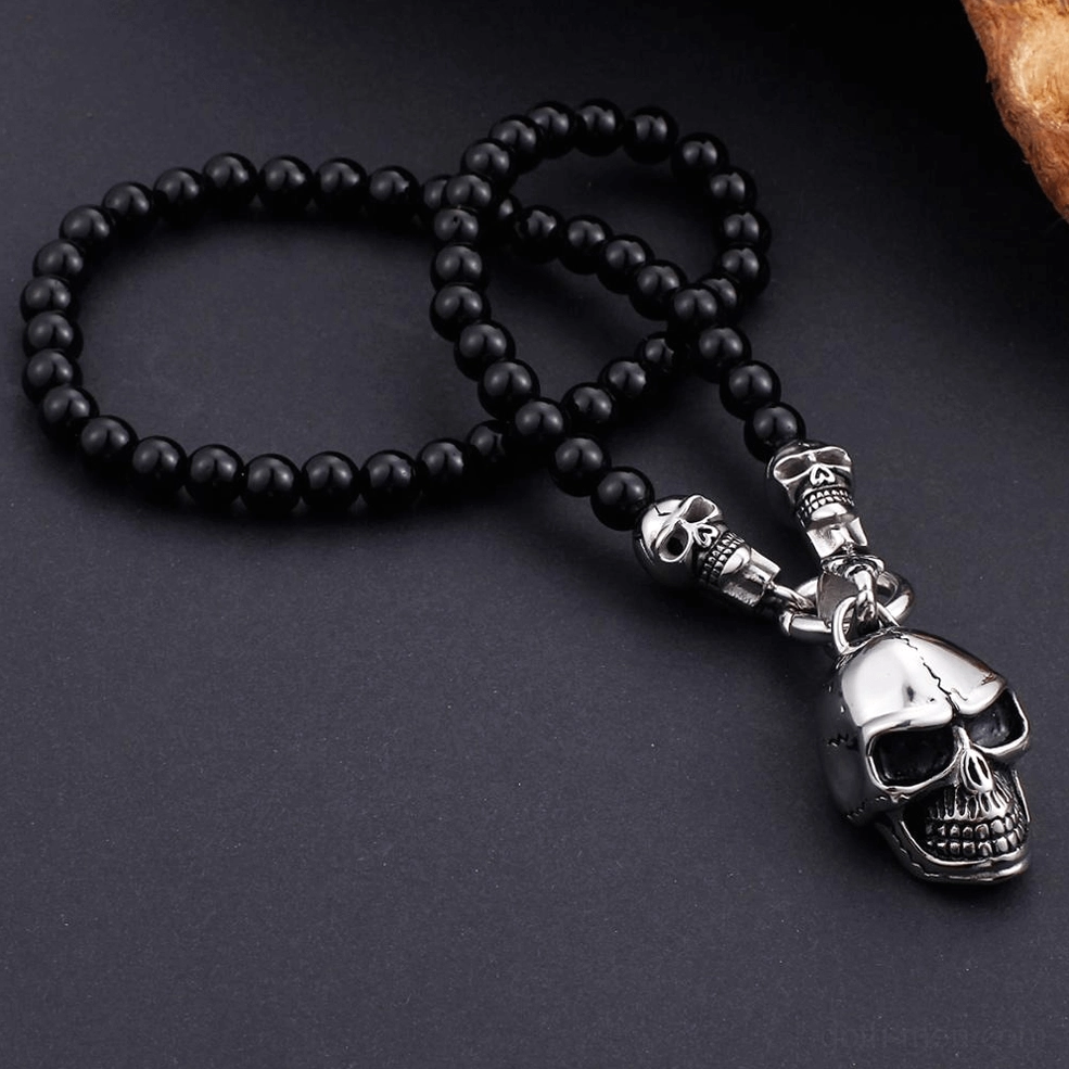 Top-down overhead flat lay black beaded gothic skull necklace dark background stainless steel