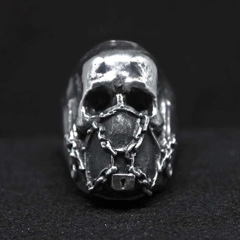 Direct frontal view of chain-locked skull ring with dark silver patina and textured metal surface