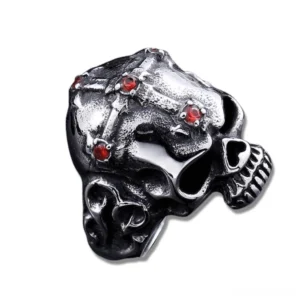 Blackened gothic skull ring with deep red gemstone accents, side three-quarter view displaying intricate cross strap design and carved jaw details