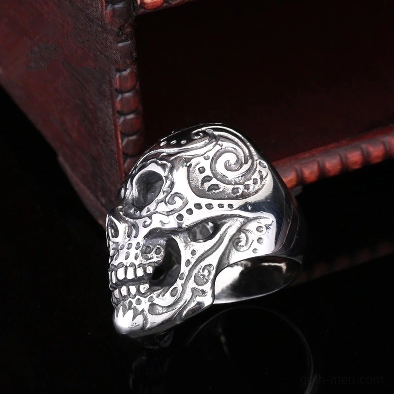 Side profile low-angle view of stainless steel skull ring with vintage wooden display box, showcasing scrollwork details