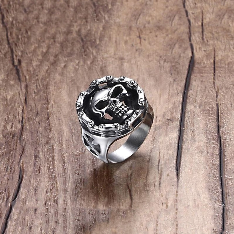 Three-quarter view of gothic skull biker ring showing studded circular frame around skull motif and polished vintage tone finish