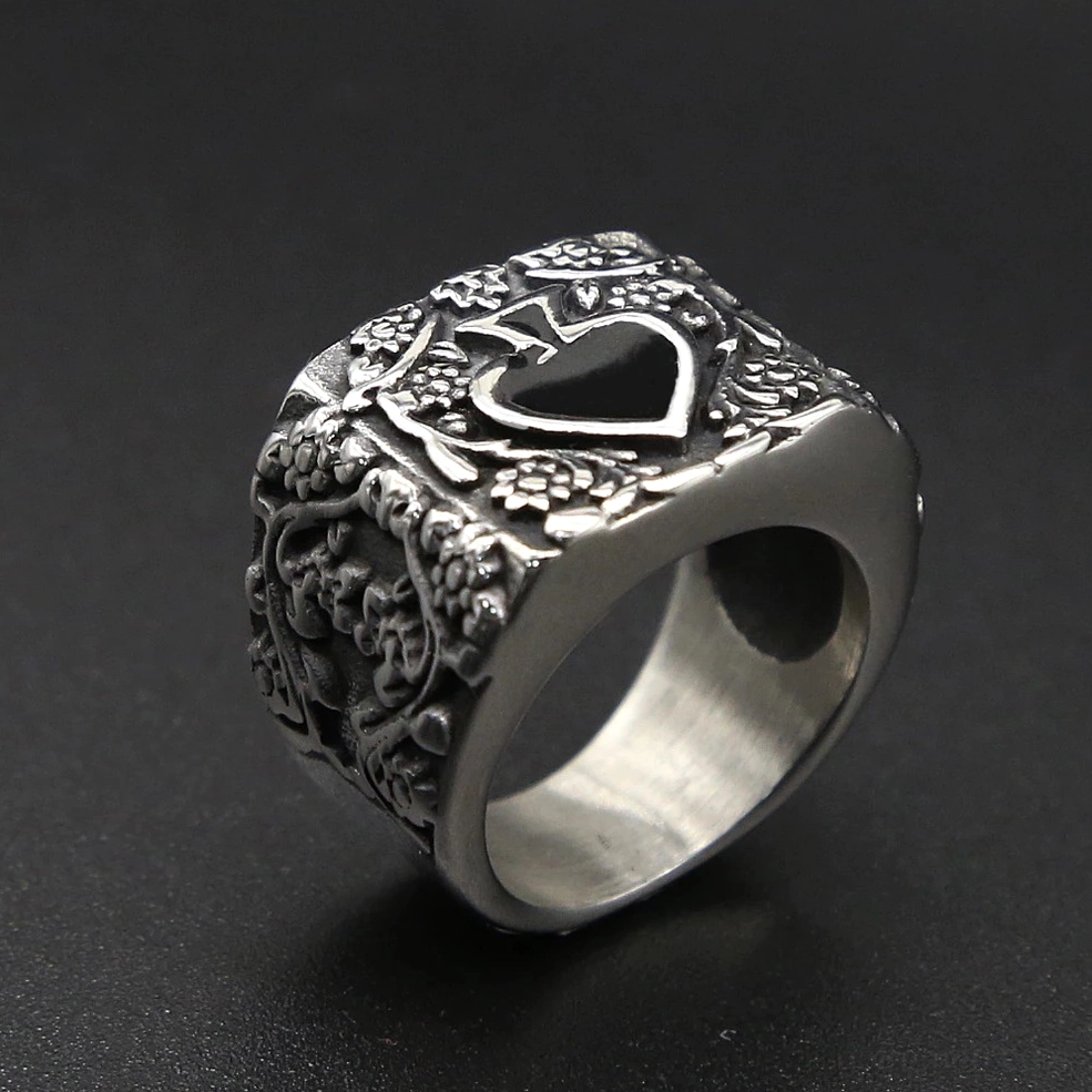 Black inlaid heart spade ring on dark grey background, three-quarter top view showing ornate embossed texture and wide silver band