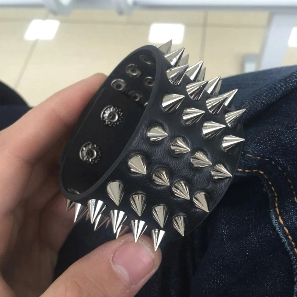 Black spiked PU leather bracelet on human wrist against denim fabric, showcasing cone-shaped metal spikes and real-world wear aesthetic
