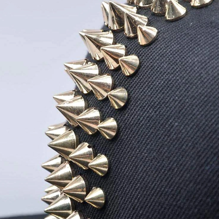 Close-up detail of gold metal spikes on black canvas gothic cap, industrial spike embellishment macro view