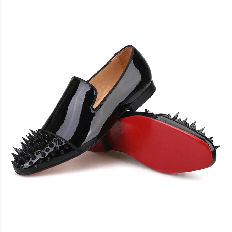 Stacked display of black patent leather spike loafers, showing geometric spike pattern on toe caps and red outsoles