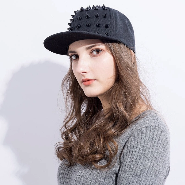 Female model wearing black spike studded gothic snapback cap with silver cone spikes, styled with grey knit sweater