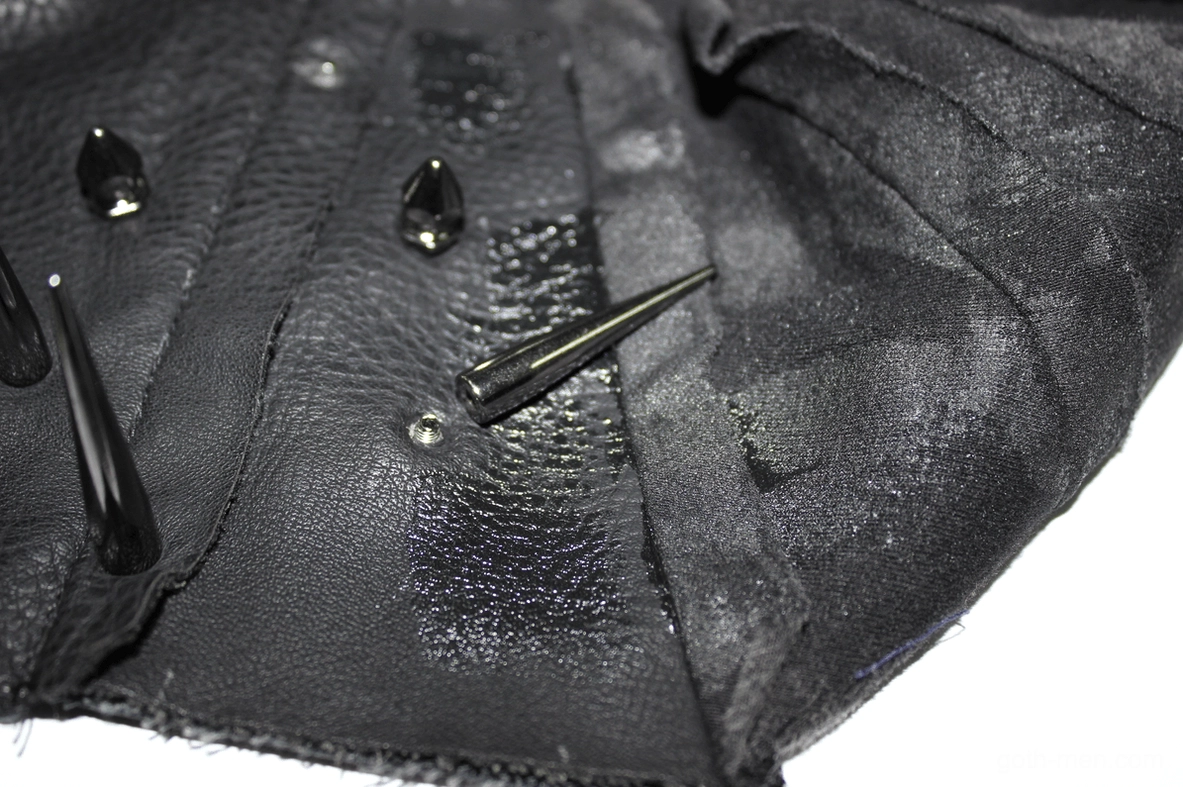 Close-up macro shot of metal spike and rivet hardware on gothic tank top, showing distressed leather texture