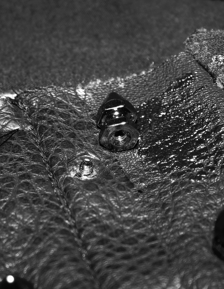 Macro detail shot showing metal rivet fastening and distressed black fabric of spike tank