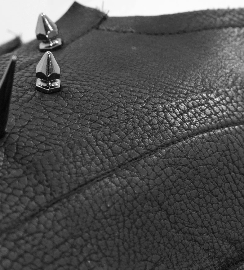 Macro close-up of black pebbled leather fabric with cone-shaped metal studs and spikes