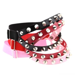 Multiple adjustable spiked knee garter belts displayed in studio flat lay, showcasing mixed metal studs and color variety for gothic aesthetic