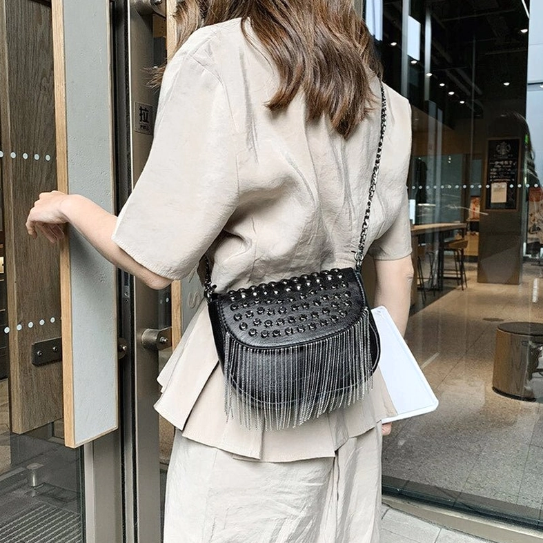 Female model wearing black gothic studded fringe shoulder bag as crossbody style, back view in indoor cafe setting