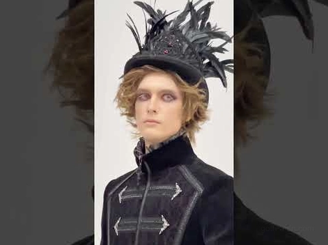 Close-up front view of gothic black tailcoat with stand collar and embroidered placket on model with feather hat