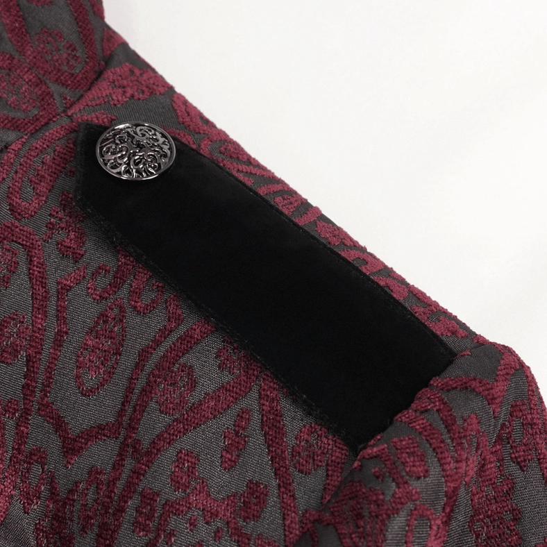 Close-up side view of black velvet decorative strap on wine red gothic tailcoat showing damask fabric base and engraved metal button fastener