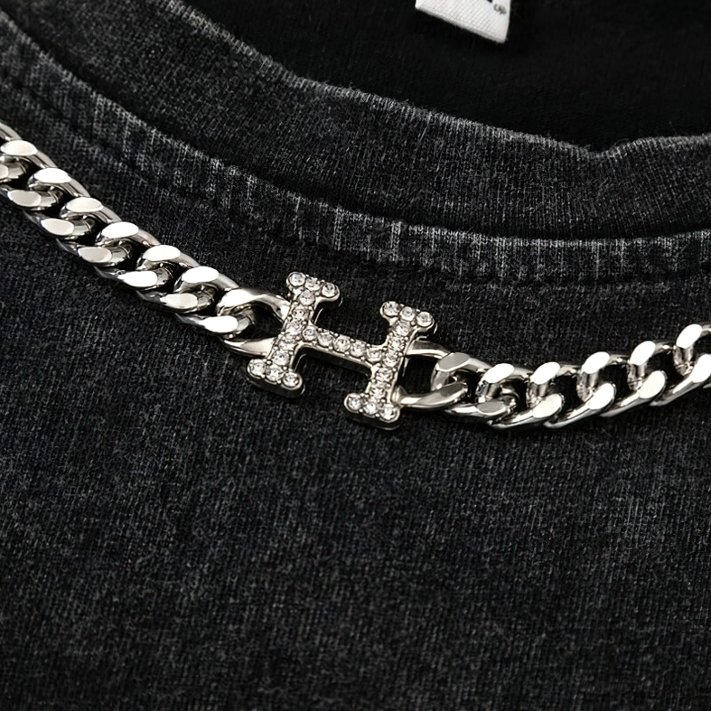 Macro close-up of rhinestone-encrusted H pendant on silver curb chain neckline detail