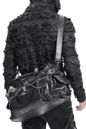 Male goth style model carrying black chain embellished gothic tote bag crossbody, back view showing strap adjustment