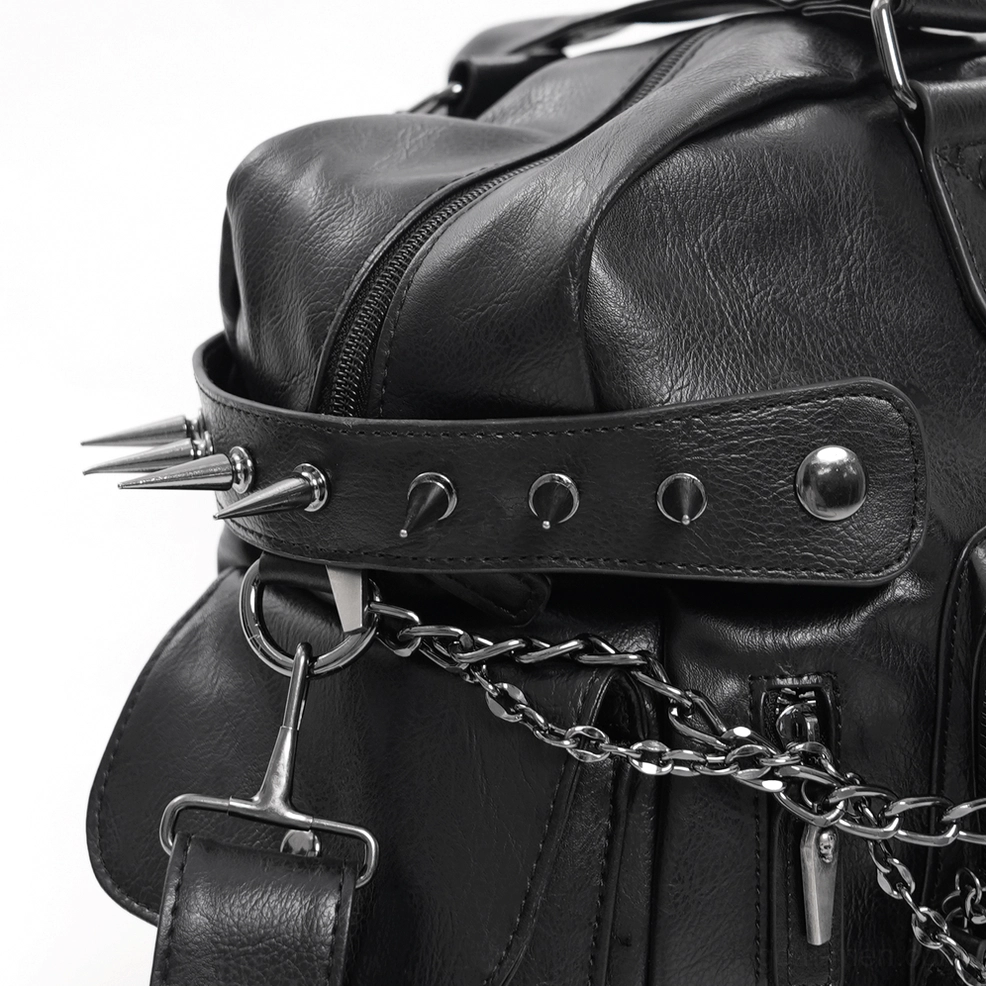 Close-up side view of black gothic tote bag showing metal spike studs, reinforced leather strap, and polished chain hardware