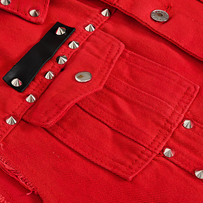 Close-up of red denim vest chest pocket area with silver cone studs and black fabric patch decoration