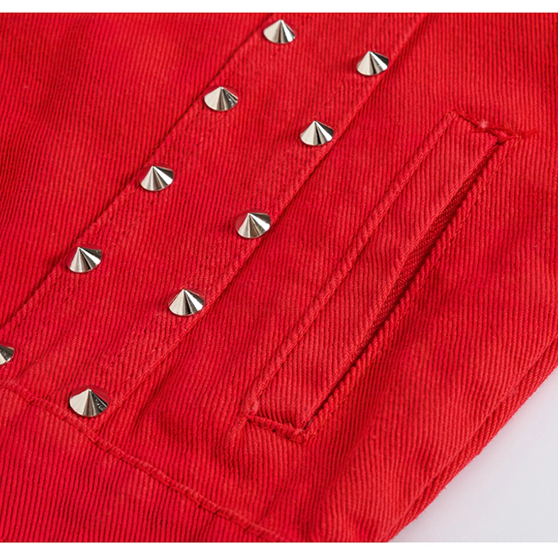 Close-up of red denim vest side pocket showing silver cone stud row decoration and twill fabric texture