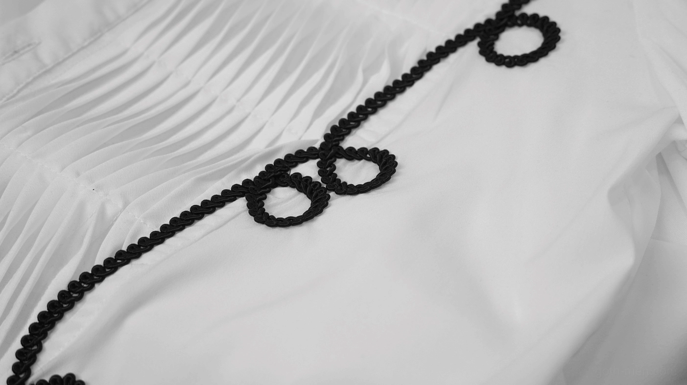 Close-up of white gothic shirt front panel showing black braided scroll embroidery and pleated fabric detail