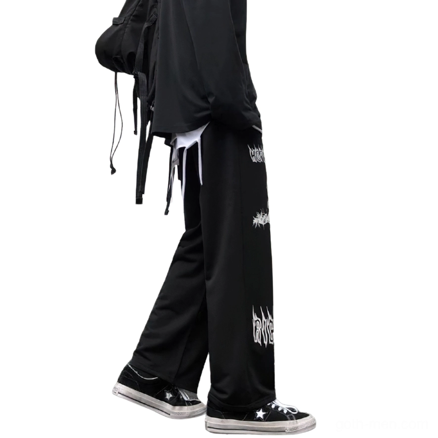 Male model rear view wearing black gothic wide leg pants with white cross print and backpack