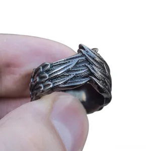 Close-up side view of dark gray stainless steel wings ring held in hand, displaying embossed feather vein texture and gothic aesthetic
