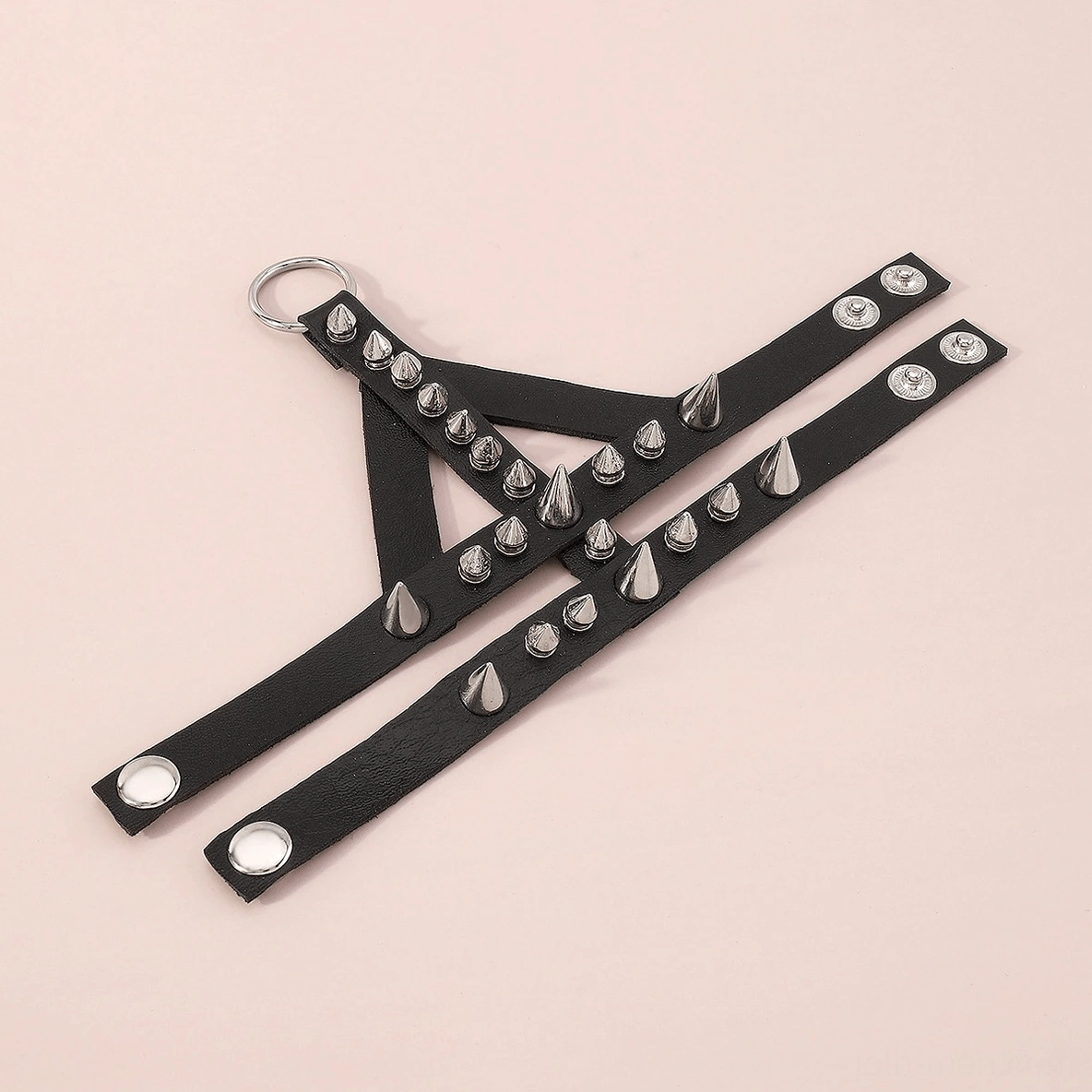 Top-down flat lay view of two-strap spiked hand bracelet with round silver metal studs on pink studio background