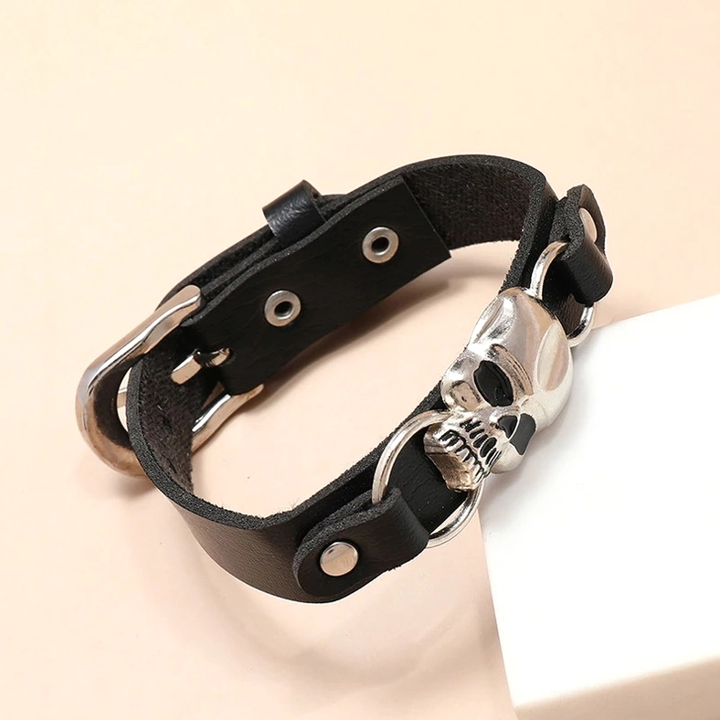 Black leather skull bracelet with silver metal closure, low-angle 3/4 view on peach background