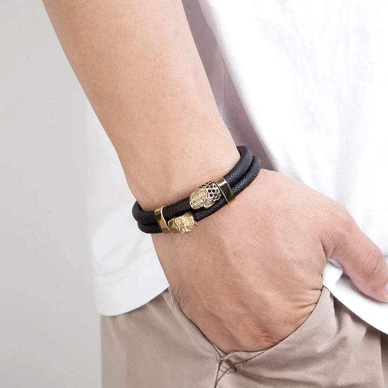 Male model wearing black leather magnetic skull bracelet with gold-tone skull decoration, wrist close-up with casual outfit