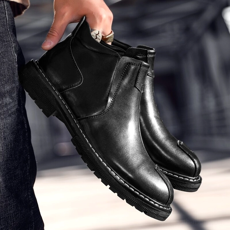 Man wearing black leather gothic Chelsea boots with dark jeans, outdoor urban setting, low angle view