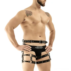Black faux leather adjustable thigh-waist harness for men with metal D-rings, front view on tattooed male model, white studio background