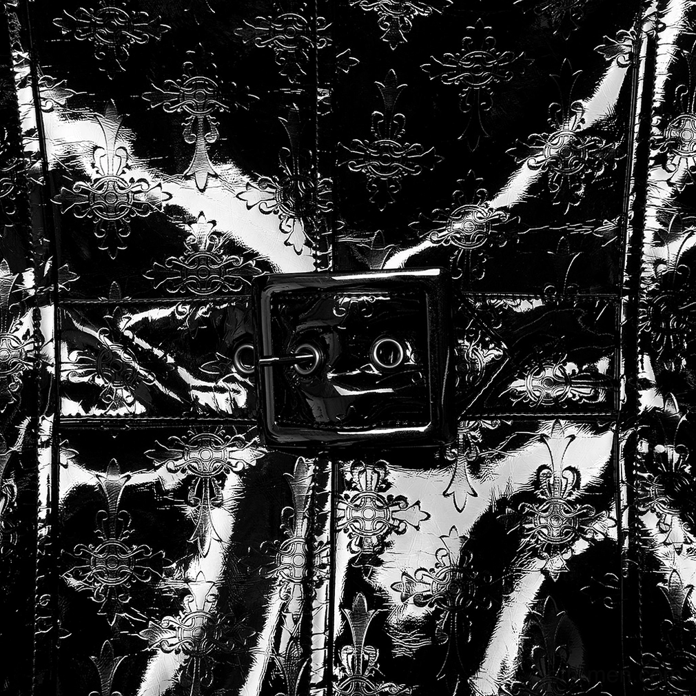 Close-up of black patent leather embossed cross patterns, square belt buckle, and glossy leather finish