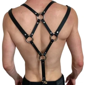 Men's black PU leather chest harness with crisscross back straps and silver metal O-rings, rear view on shirtless muscular male model