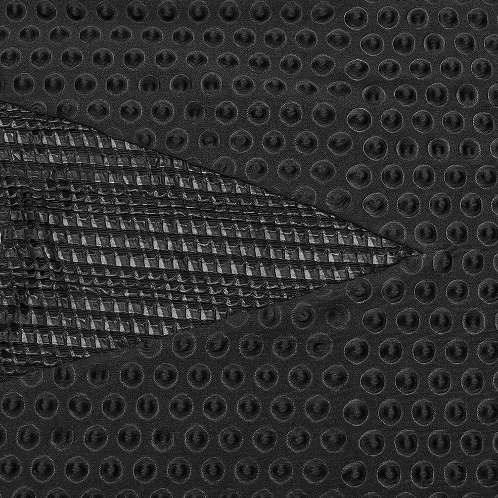 Magnified view of perforated circular mesh texture and woven accent panel on black gothic tactical tee fabric