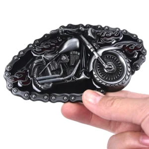 Hand holding motorcycle themed belt buckle, side oblique angle displaying the embossed bike design and ornamental chain framing with red flame accents